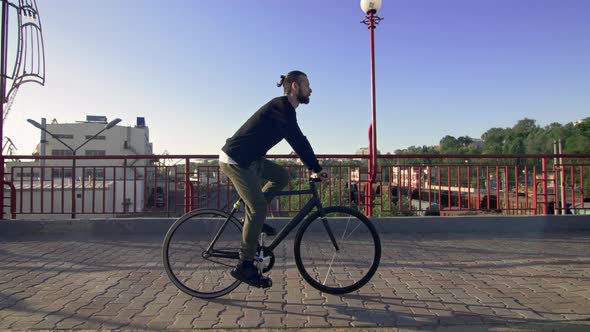 Stylish Handsome Man Riding Bicycle During Sunset or Sunrise with Sea Port on Background