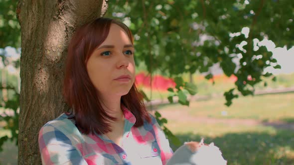 Close Up of Young Woman Rests Sitting Near Tree in Parkland