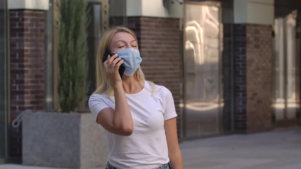 Portrait of Pretty Young Woman in Protective Medical Mask Is Talking on Her Smartphoneis. COVID-19