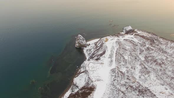 View From a Drone on a Snowcovered Rocky Seashore at Sunset