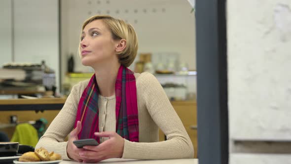 Upset woman with mobile phone waiting at table in cafe. 