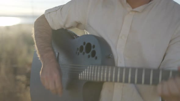 Hispanic Man Playing Guitar and Singing Against Sun Light Outdoors