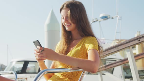 Side view of a teenage Caucasian girl enjoying her time on a boat and using her phone