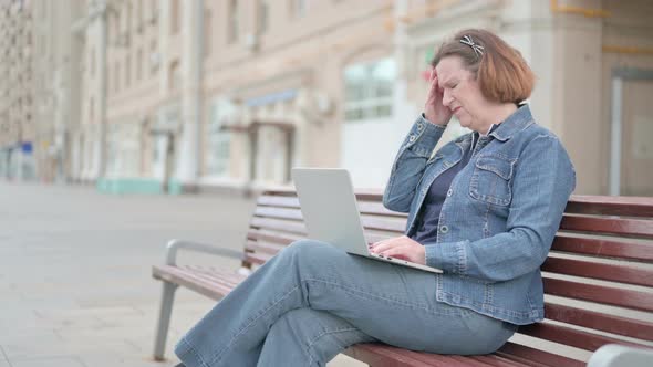 Old Woman with Headache Using Laptop While Sitting Outdoor on Bench