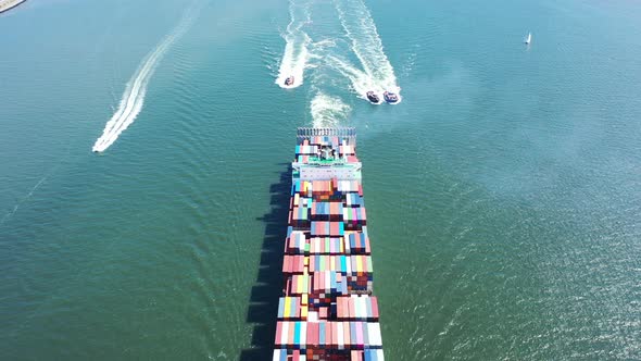 An aerial shot of a cargo ship with colorful containers on-board. The drone dolly in & tilt up as it