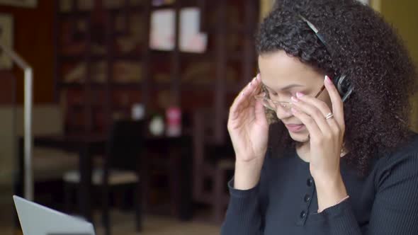 African American Woman Tired While Working on Laptop. She Takes Off Her Glasses and Massages the