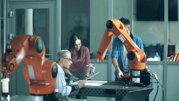 Cheerful People Work with Robotic Arm on a Table. Modern Science Laboratory.