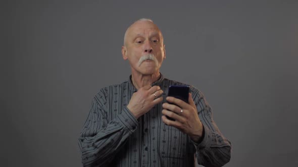 Man Holds Telephone Looks at Screen and Straightens Shirt