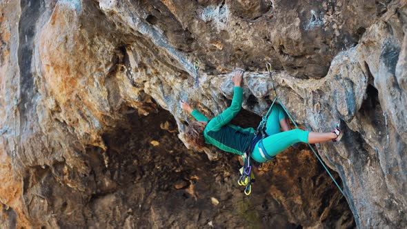 Strong Woman Rock Climber Climbs Hard Tough Rock Route on Very Overhanging Black Cliff in Cave