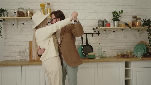 Beautiful Longhaired Wife Dancing with Her Young European Husband in the Kitchen Celebrating Their