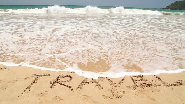 I LOVE TRAVEL written in the beach sand washed aways by waves.