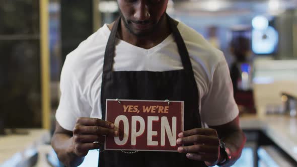 Portrait of happy african american barista holding 'we're open' sign in cafe