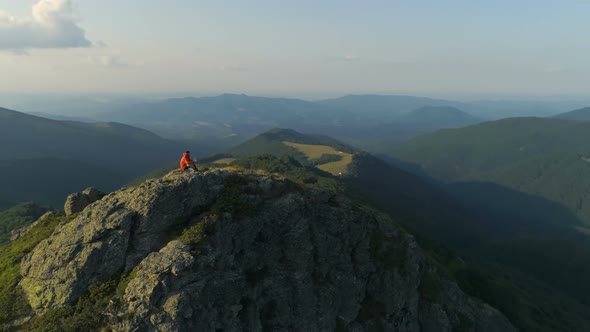 Male Hiker Sitting on Top of Rocky Mountain Peak Looking Down the Deep Valley