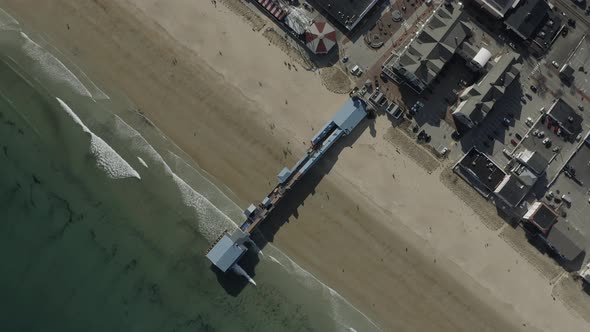 Top down drone shot, panning right and flying down, showing a pier on a beach.