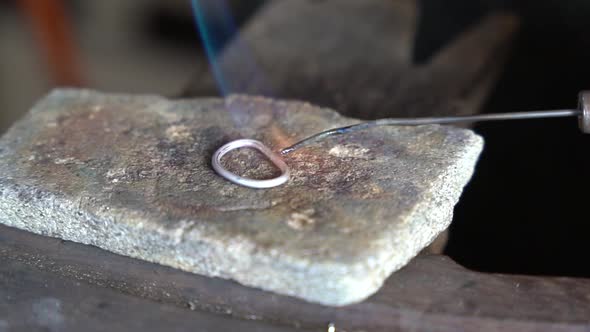 Torch heating and melting precious metal ring for creating an art piece, Close up view