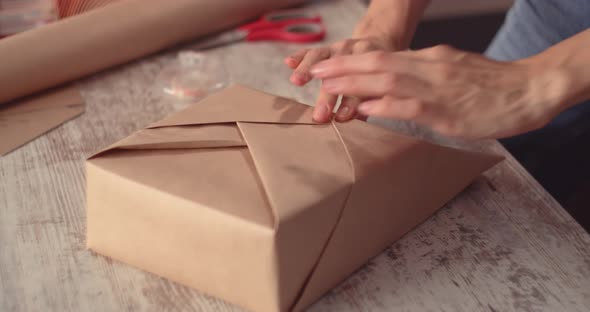 Woman wrapping holyday gift, decorating stylish gift in craft paper