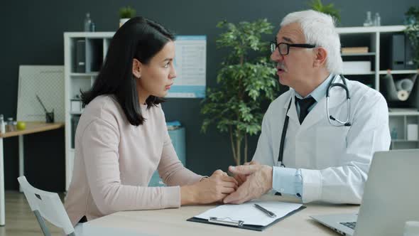 Caring Doctor Talking To Young Woman Holding Hand Expressing Support and Care in Office