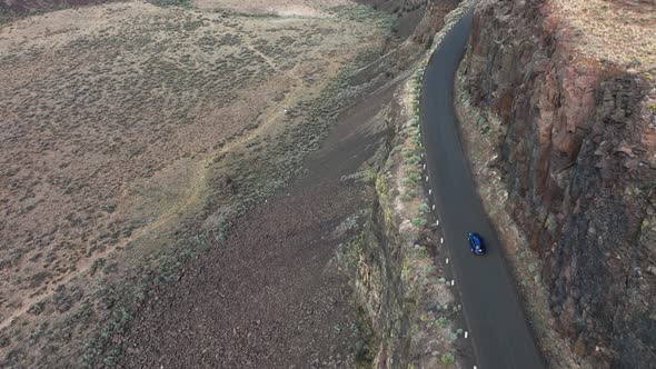 Aerial of a blue SUV driving along a cliff in Washington's desert region.