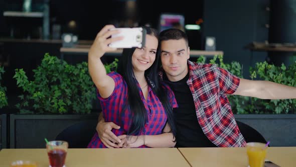 beautiful couple in plaid shirts are sitting at the table and taking selfies. Dating in the cafe