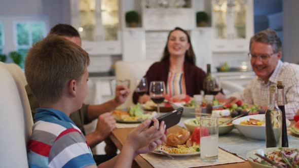 Happy caucasian grandson taking selfie with parents and grandfather at table during family meal