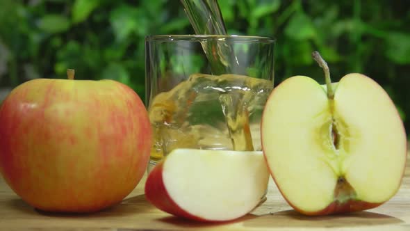 Juice Is Poured in a Glass Next To Apple Slices on the Background of Greenery