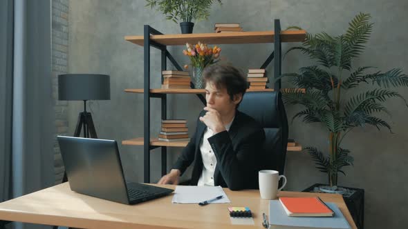 Young Handsome Businessman Fills Out Financial Statements While Sitting in His Office