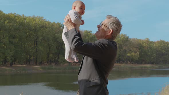 Grand-father Holding Baby Infant in Arms Outside. Grand Parent Bonding with Grand-child.