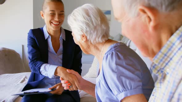 Caucasian female real estate agent shaking hands with senior couple at home 4k