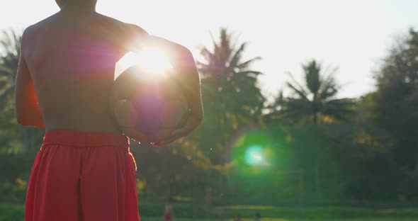 Rural Boy Without Shirt Holding Old Soccer Ball With Sun Sight