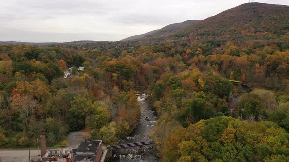 An aerial shot of the colorful fall foliage in upstate NY. The camera dolly in over a black river wi
