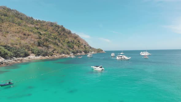 Yachts and Crystal clear blue waters surrounding the steep hill bordering the shore in Ko Racha Yai