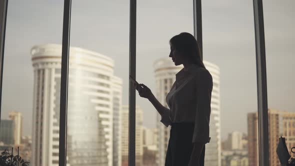 Businesswoman Silhouette with a Mobile Phone in Hand. Girl Uses a Smartphone in the Office