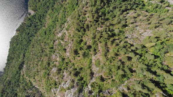 Aerial: steep hillside cliff descending down to lake, highland landscape