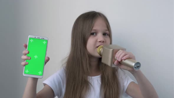 Little Girl Shows Phone with Green Screen Mock Up and Singing Song in Wireless Karaoke Microphone