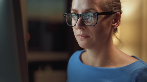 Woman in Glasses Looking on the Monitor and Surfing Internet. The Monitor Screen Is Reflected in the