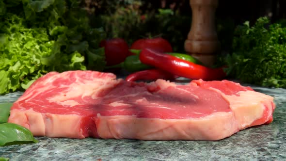 Raw Steak is Falling on a Stone Table on the Background of Fresh Vegetables