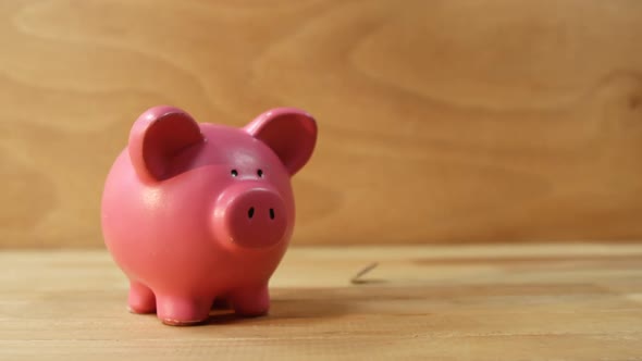 Coins falling into piggy bank against wooden background