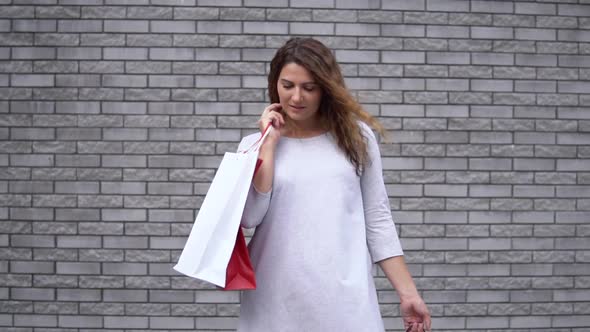 A Girl with Packages After Shopping with a Good Mood Against a Wall of Stones