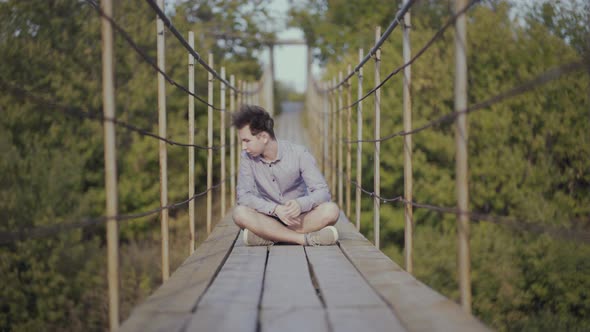 Guy Sits on Suspended Bridge in the Forest
