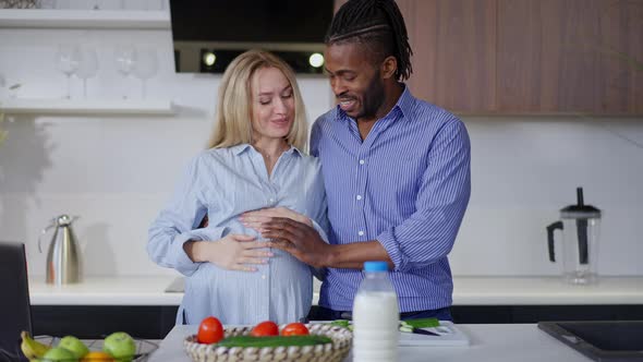 Happy Interracial Couple Standing in Kitchen Caressing Pregnant Belly