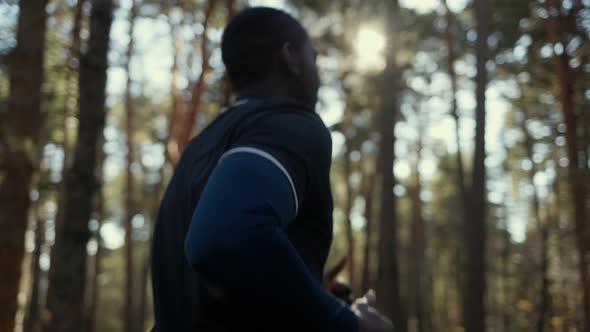 Young Fit African American Male Jogging on a Forest Road.