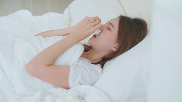 Attractive young woman lying in bedroom, feel bad and suffer from allergy then put tissue cover nose