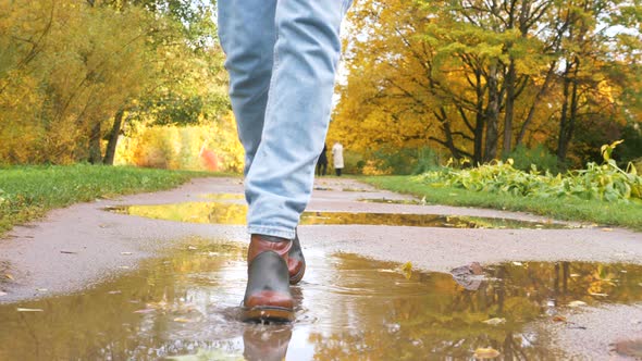 Woman in Boots Walks Along Road with Puddles in Autumn Park