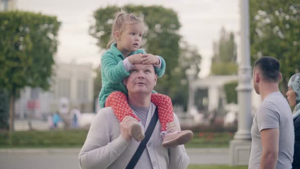 Young Dad Riding Daughter on Shoulders in Summer Park