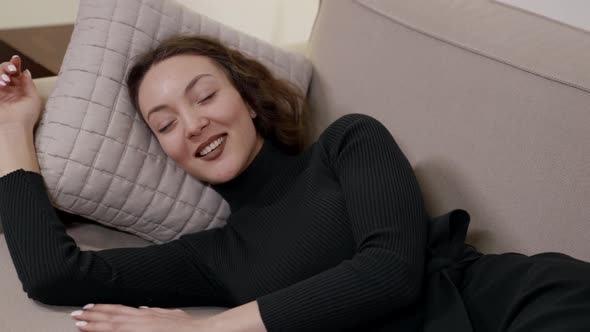 Happy Relaxed Woman Is Lying on Sofa in Living Room and Dreaming Smiling Charmingly