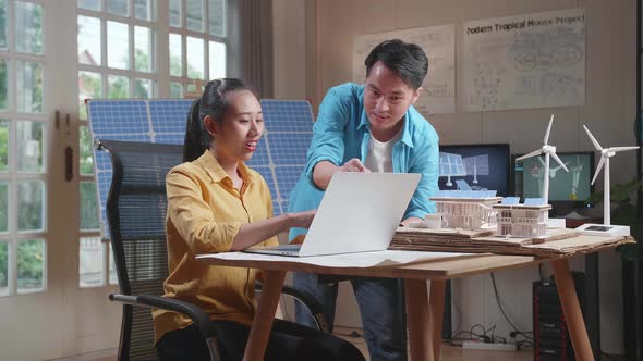 Man And Woman Discuss About Work On A Laptop Next To The Model Of A Small House With Solar Panel