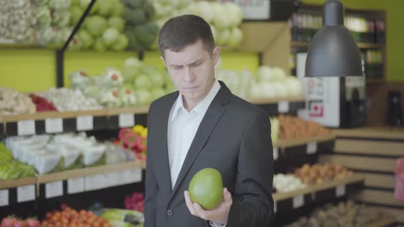 Middle Shot of Concentrated Caucasian Man Choosing Pomelo in Grocery. Portrait of Young Confident