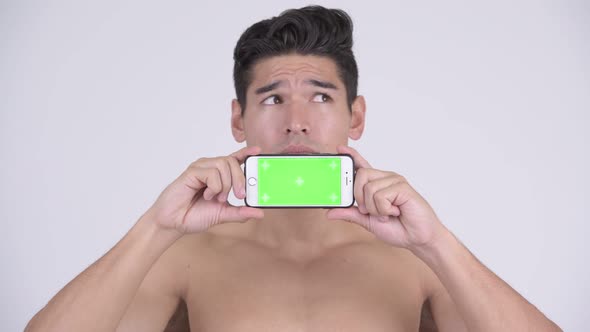Happy Young Shirtless Muscular Man Thinking While Showing Phone