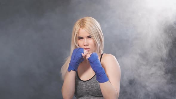 Blonde Female Athlete Is Exercising in Defense on Dark Smoky Background, Slow Motion