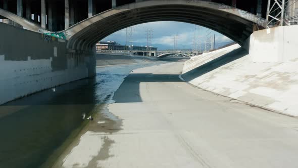 Drone Flying Under Arched Concrete Bridge Above Scenic Los Angeles River Water